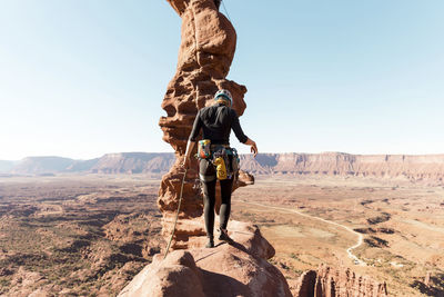 Rear view of female hiker walking on rock formation against clear sky during sunny day