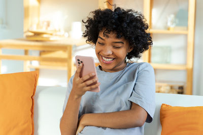 Young woman using mobile phone while sitting on bed at home