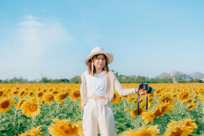 Woman standing on sunflower field against clear sky