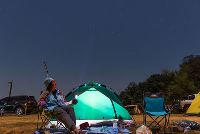 Man sitting at tent against sky at night