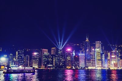 Illuminated buildings by river against sky at night