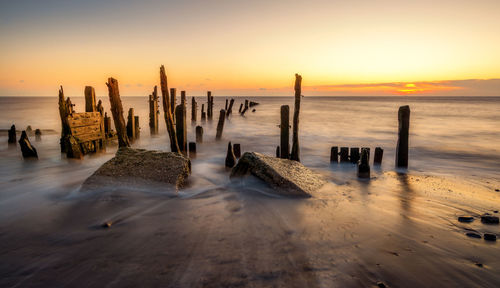 Wooden posts on beach against sky during sunset