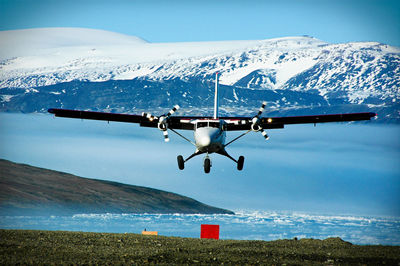 Biplane flying over lake against snowcapped mountains during sunny day