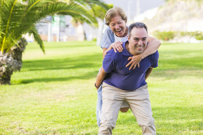 Happy son piggybacking mother on field at public park