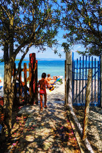 Rear view of boy playing with ball while walking towards beach