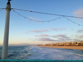 Low angle view of string lights hanging on pier at beach against sky