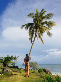 Rear view of woman on grass by sea against sky