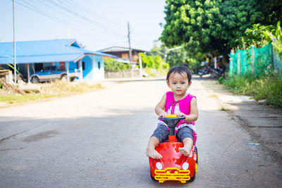 Cute girl riding toy car on road in city