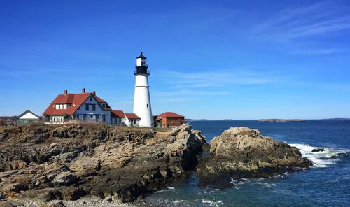 Lighthouse by sea against blue sky