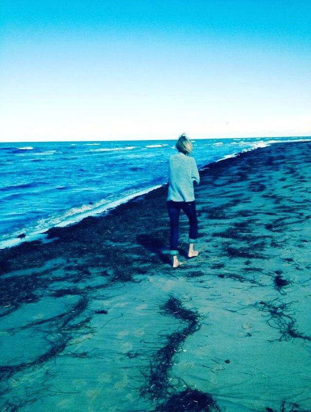 WOMAN STANDING ON BEACH AGAINST CLEAR BLUE SKY