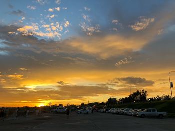 Cars on road against dramatic sky during sunset