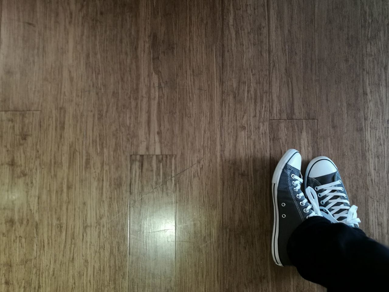 LOW SECTION OF MAN WEARING SHOES ON WOODEN FLOOR