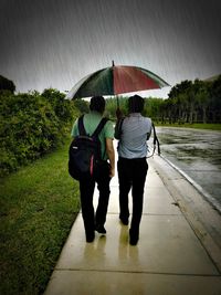 Rear view of people walking on wet road during rainy season