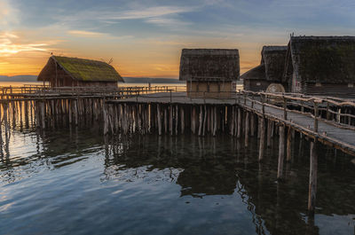 Wooden posts in sea against sky during sunset