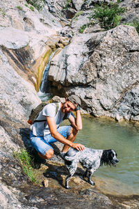 Male owner of spaniel dog walking against mountains and waterfall background.