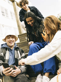 Low angle view of male and female friends sharing smart phone while sitting on steps