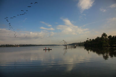 Scenic view of boat in lake by tree against cloudy sky