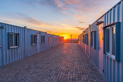 Empty footpath amidst buildings against sky during sunset