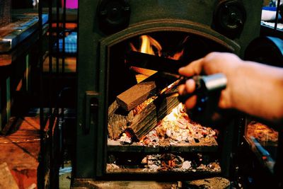 Cropped hand burning wood in fireplace at home