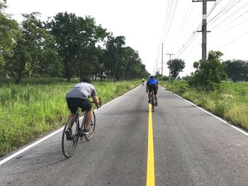 Rear view of men riding bicycles on road
