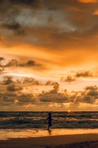 Silhouette woman on beach against sky during sunset