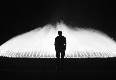 Rear view of silhouette man standing in front of fountain at night