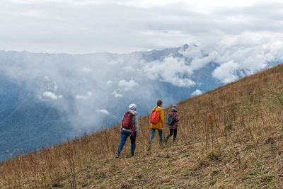 Rear view of people walking on field against sky