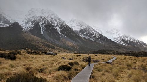 Rear view of man walking on boardwalk towards mountains