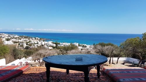 Empty chairs and table by sea against clear blue sky