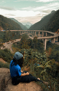 Young women wearing hat sitting on cliff against road