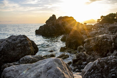 Rocks on sea shore against sky during sunset