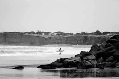 Man with surfboard walking at beach against clear sky