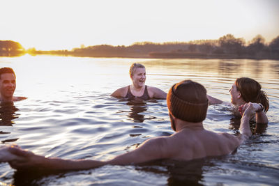 Women with male friends laughing while enjoying in cold water during morning