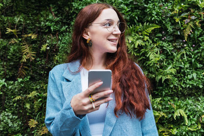 Attractive business woman smiling and holding mobile phone while looking away, empty space for text