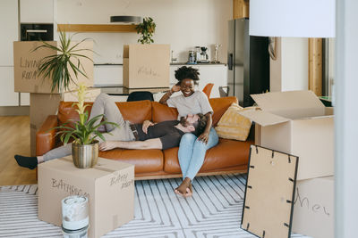 Happy multiracial couple having fun while sitting on sofa in living room at new home