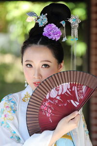 Portrait of young woman wearing qipao while holding hand fan