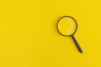 Directly above shot of magnifying glass on yellow background
