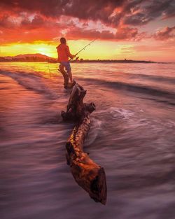 Rear view of man fishing in sea during sunset