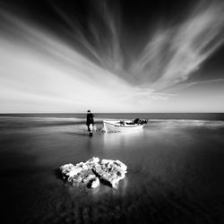 Man with boat on shore at beach against sky