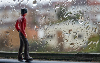 Woman standing on wet glass window in rainy season