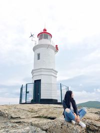 Woman sitting on lighthouse against sky