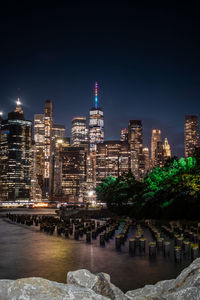 Illuminated buildings by river against sky at night