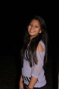 Portrait of smiling young woman against black background