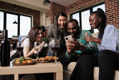 Portrait of smiling friends using smart phone while sitting at restaurant