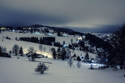 High angle view of houses and trees on snow covered field against sky at dusk