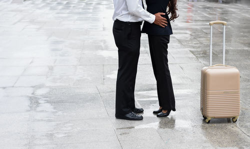 Low section of couple standing by luggage on footpath