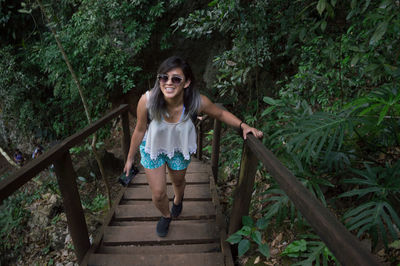 Portrait of smiling young woman wearing sunglasses while walking on staircase