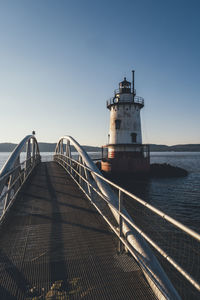 Bridge over sea by lighthouse against clear sky