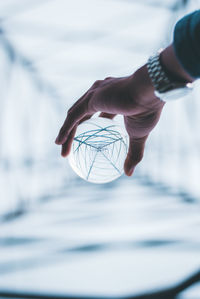 Cropped hand holding crystal ball with reflection of electricity pylon