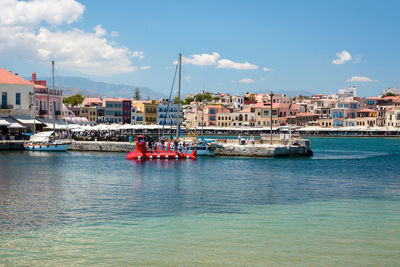 Sailboats in sea by buildings against sky